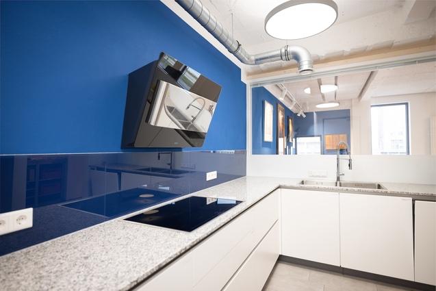 Moderne K&uuml;che mit grauem Granit-Arbeitsplatz, blauer Wand und einem Wandherd &uuml;ber dem Kochfeld.