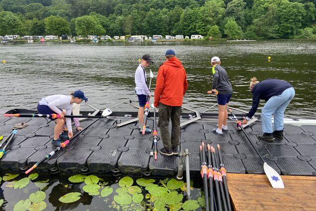 Gruppen von Ruderern am Steg, während sie Boote und Ruder für das Training an einem See vorbereiten.