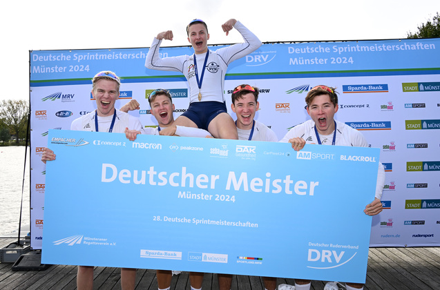 Gruppe jubelnder Ruderer h&auml;lt ein Schild mit der Aufschrift &bdquo;Deutscher Meister M&uuml;nster 2024&ldquo; nach dem Rennen.